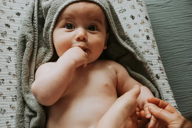Un bébé emmailloté dans une serviette grise, détendu après sa séance de baby spa